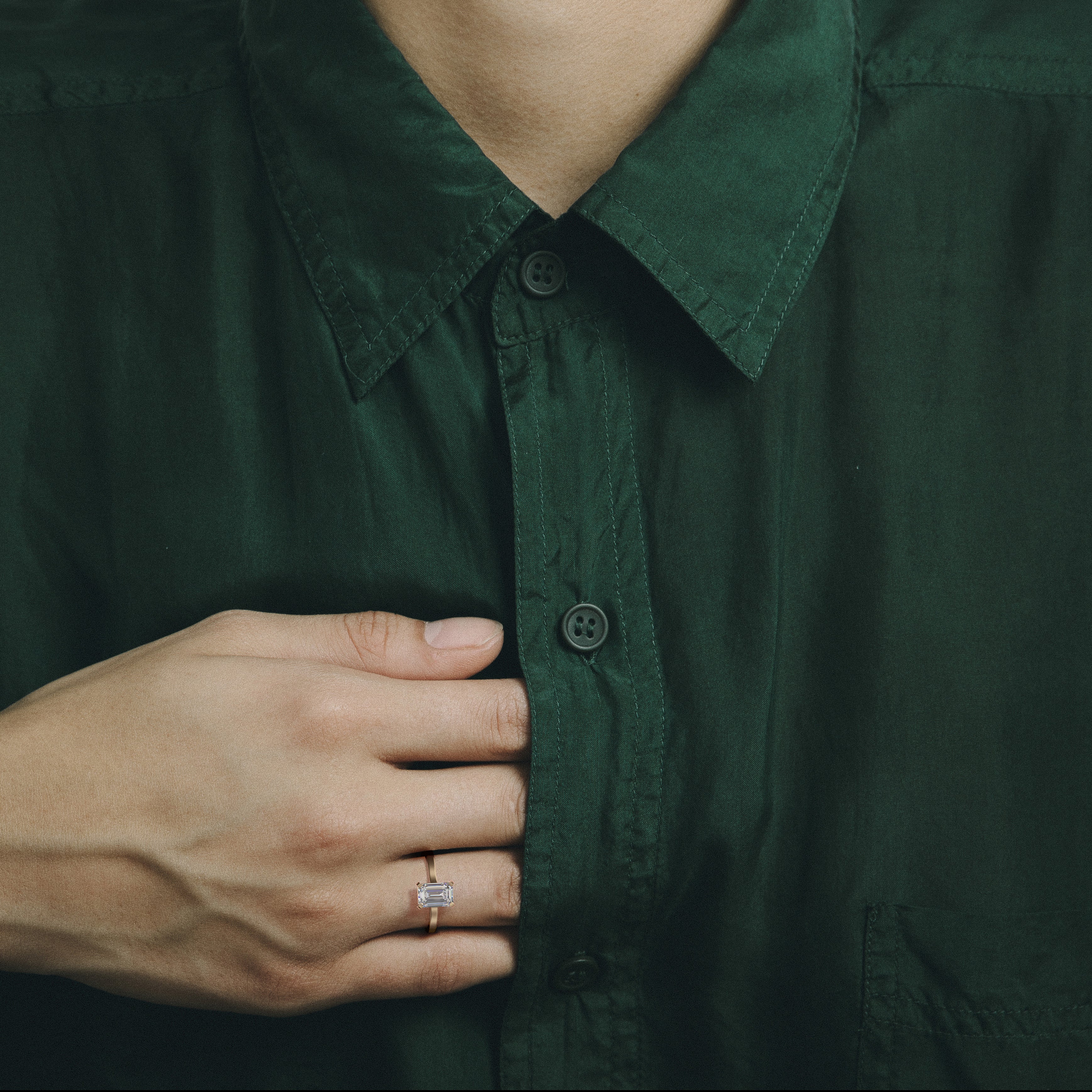 Dainty yellow gold engagement ring with emerald-cut diamond worn on hand