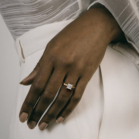 Dainty yellow gold engagement ring with princess-cut diamond worn on hand