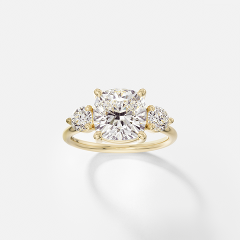 14k yellow gold three stone engagement ring with 3.25 carat cushion-cut diamond in corner prongs and round side stones on delicate round band