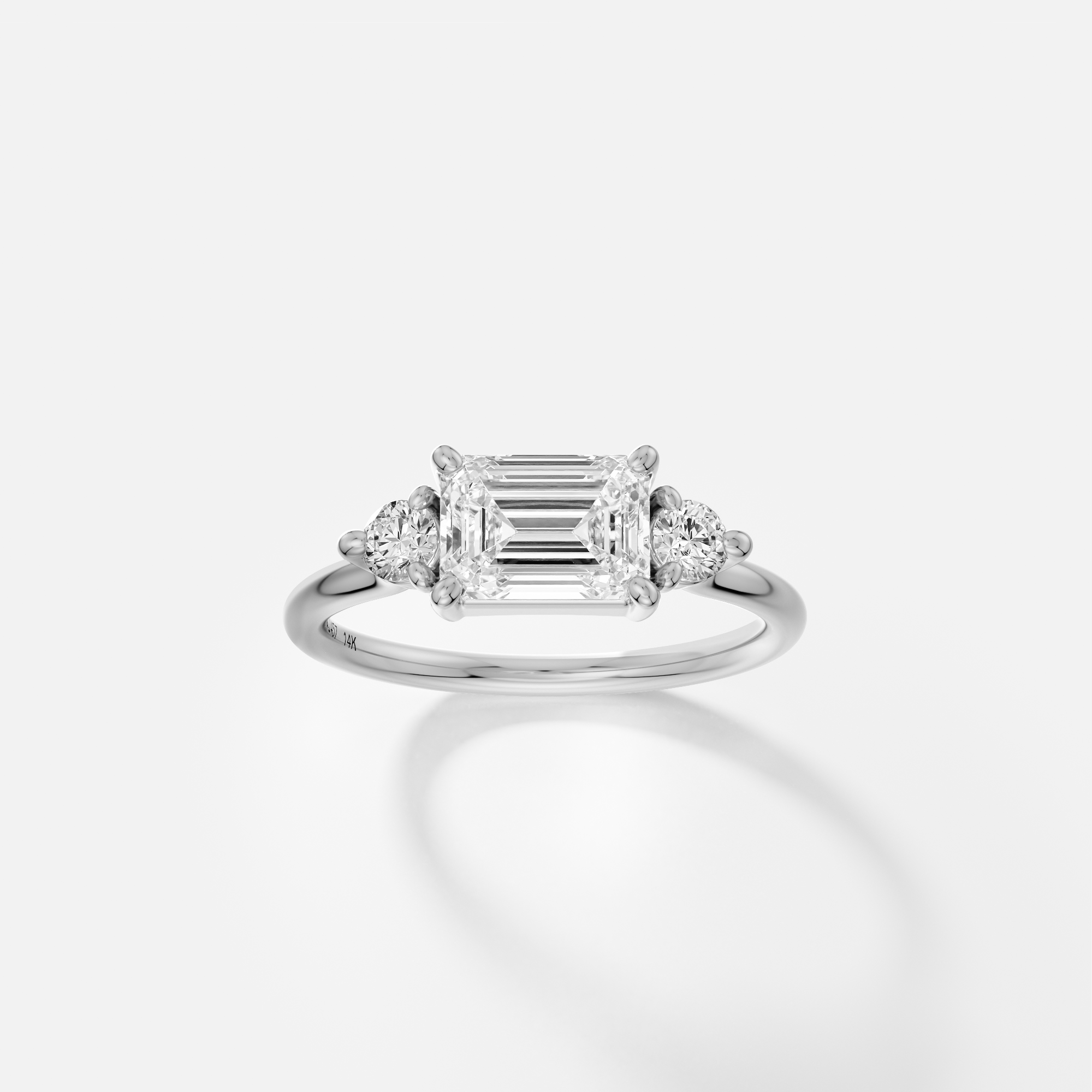 Platinum engagement ring with emerald-cut diamond set east-west and round side stones in corner prongs on delicate band