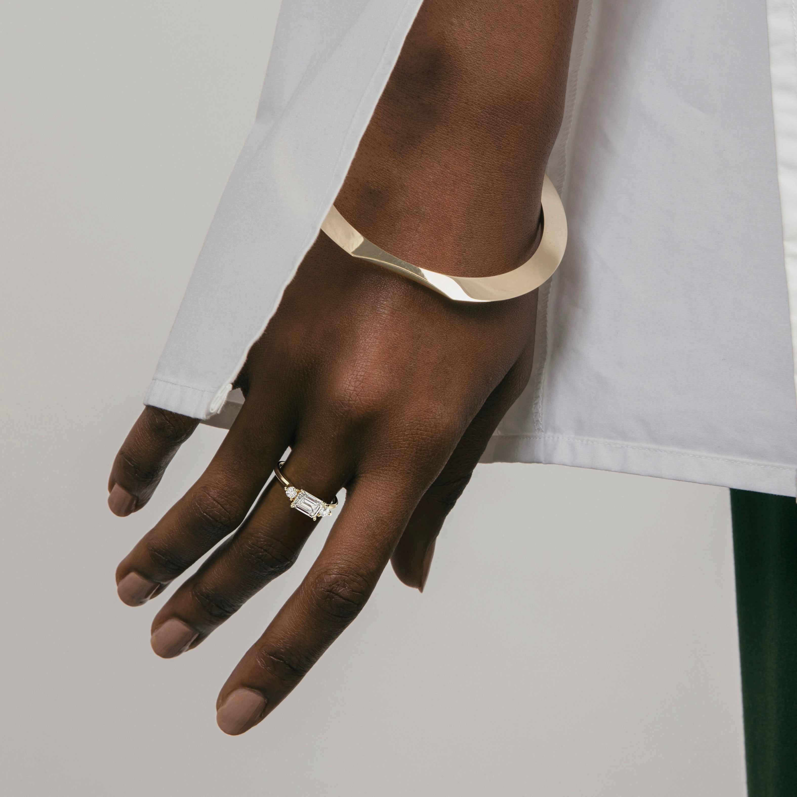 14k yellow gold three stone engagement ring with emerald-cut diamond and round side stones worn on hand