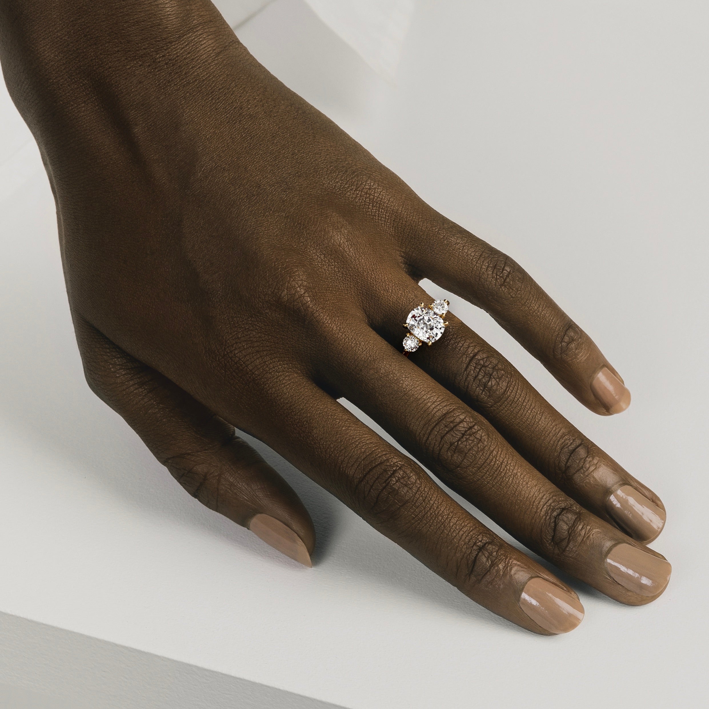 14k yellow gold three stone engagement ring with elongated cushion diamond and round side stones worn on hand