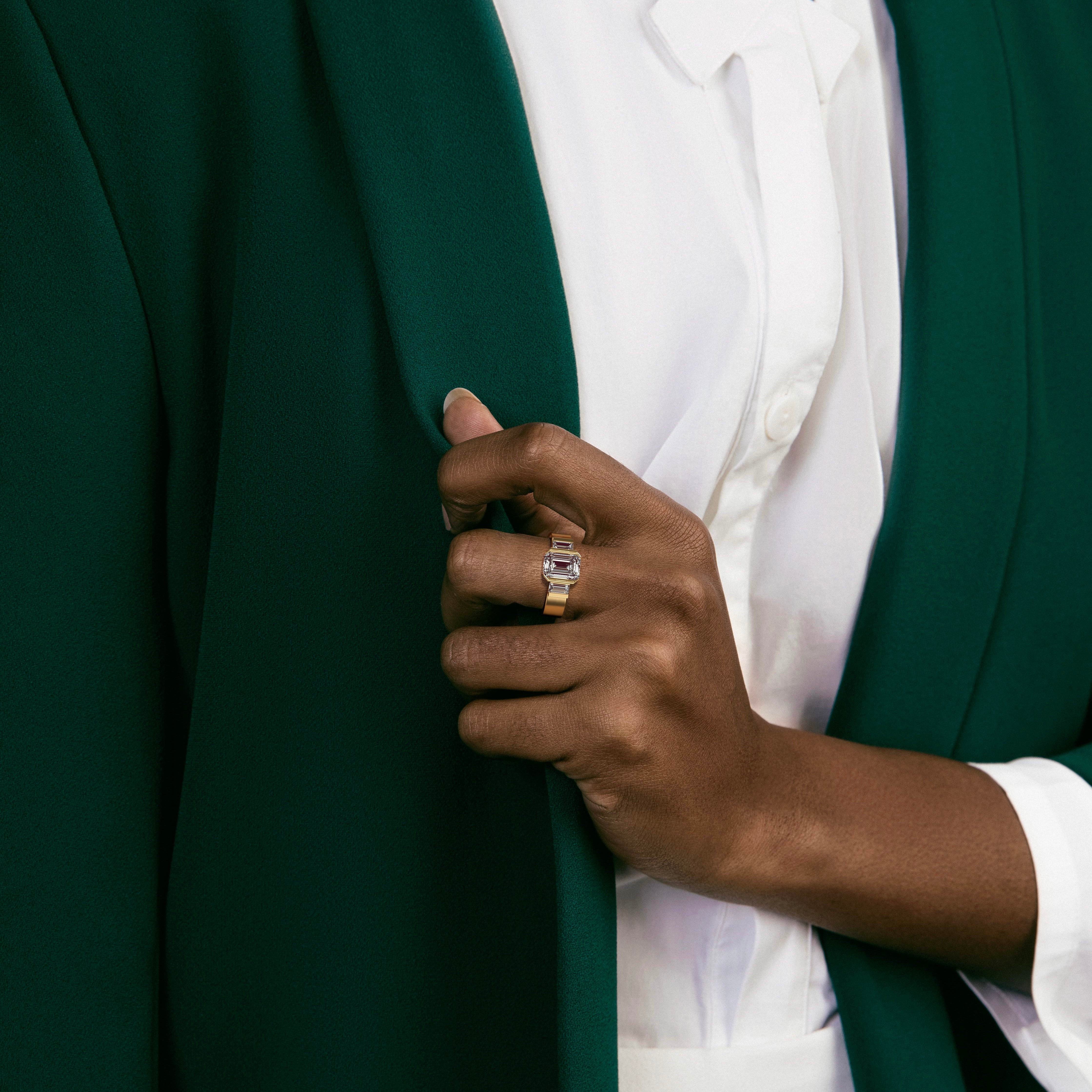 emerald-cut diamond three stone engagement ring with baguette side stones in partial bezel worn on hand