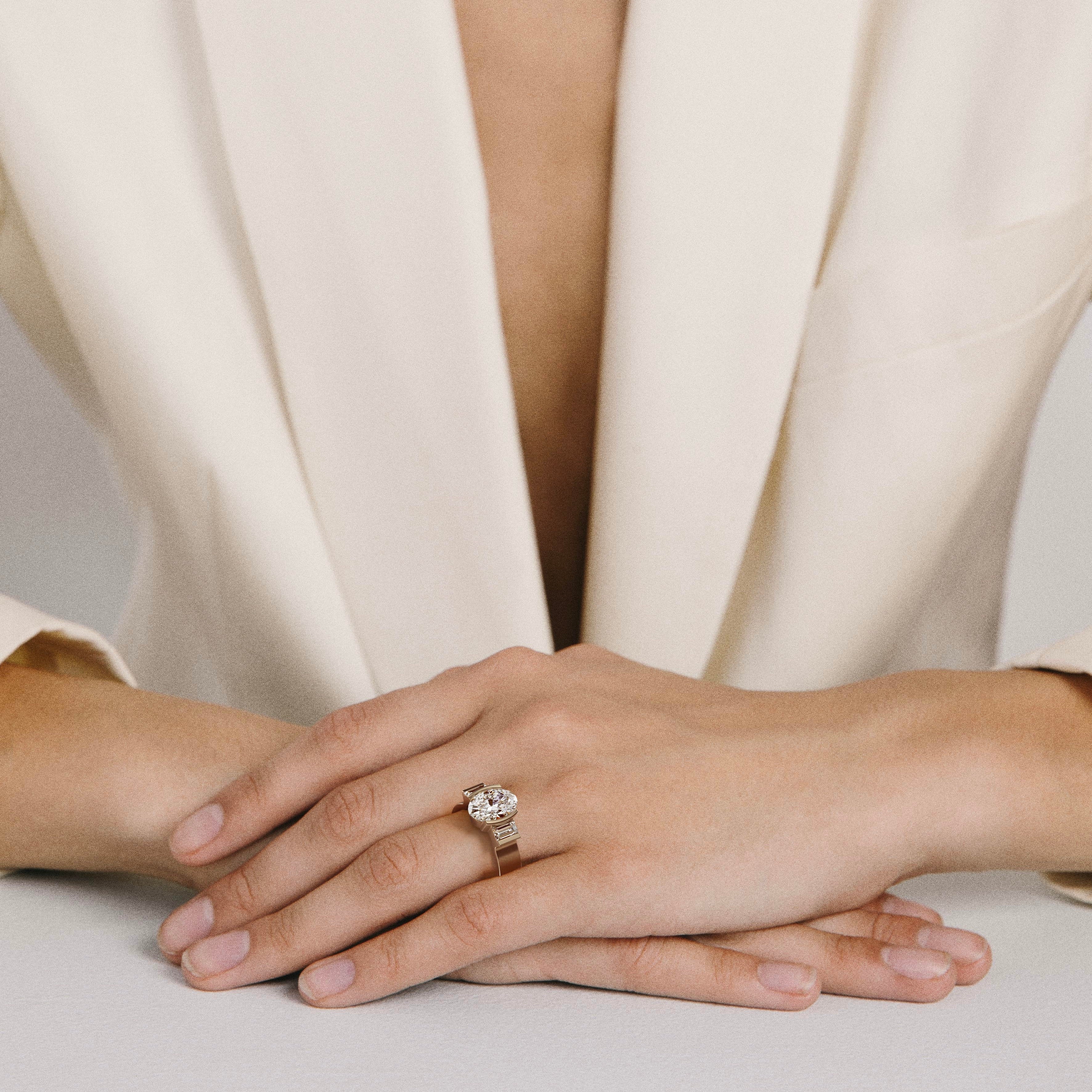 oval diamond three stone engagement ring with baguette side stones in partial bezel worn on hand