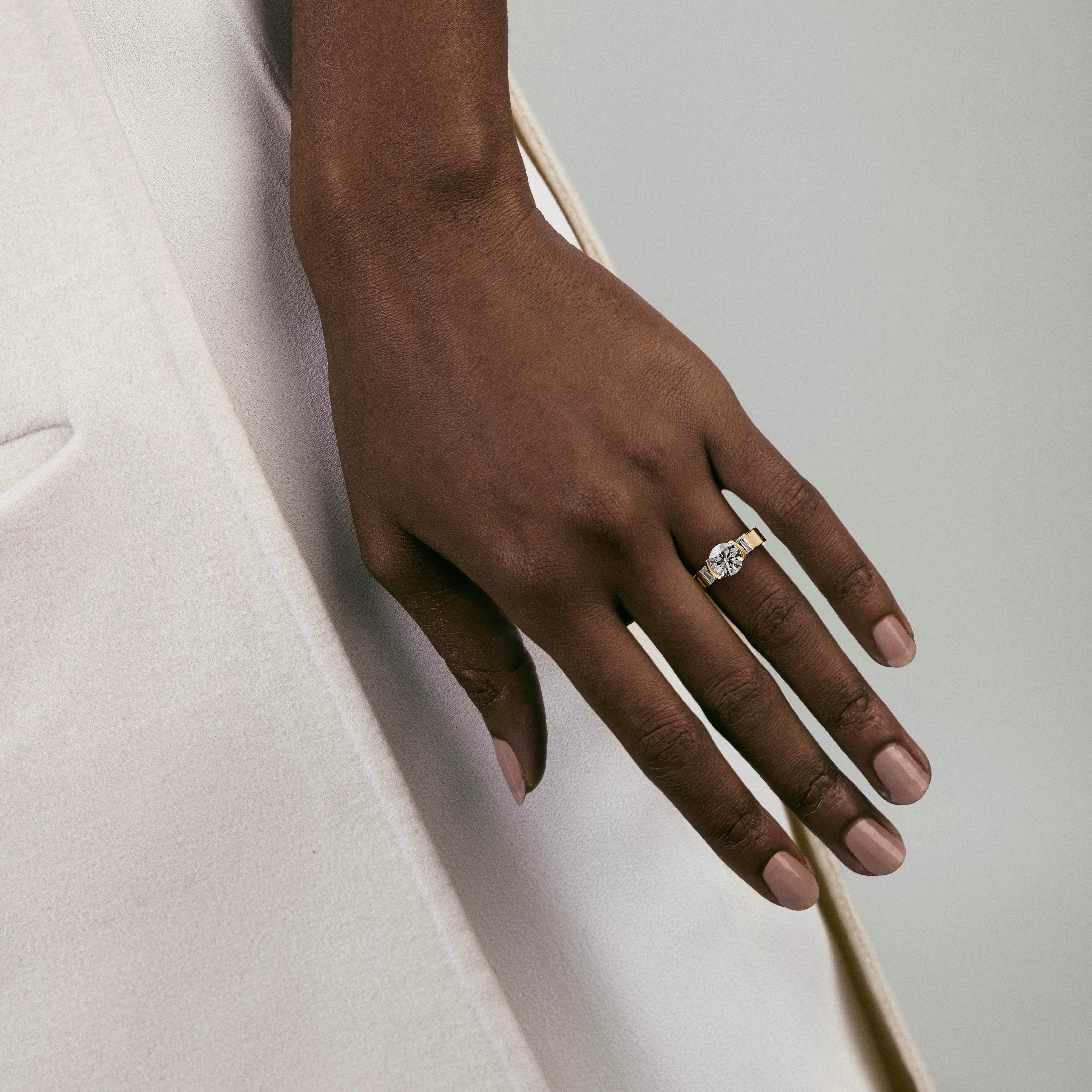 round brilliant diamond three stone engagement ring with baguette side stones in partial bezel worn on hand