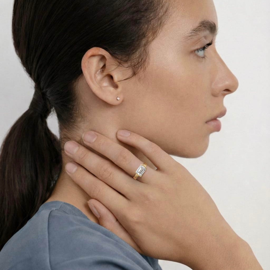 close view of east-west emerald-cut diamond engagement ring with tapered partial bezel and narrowing band