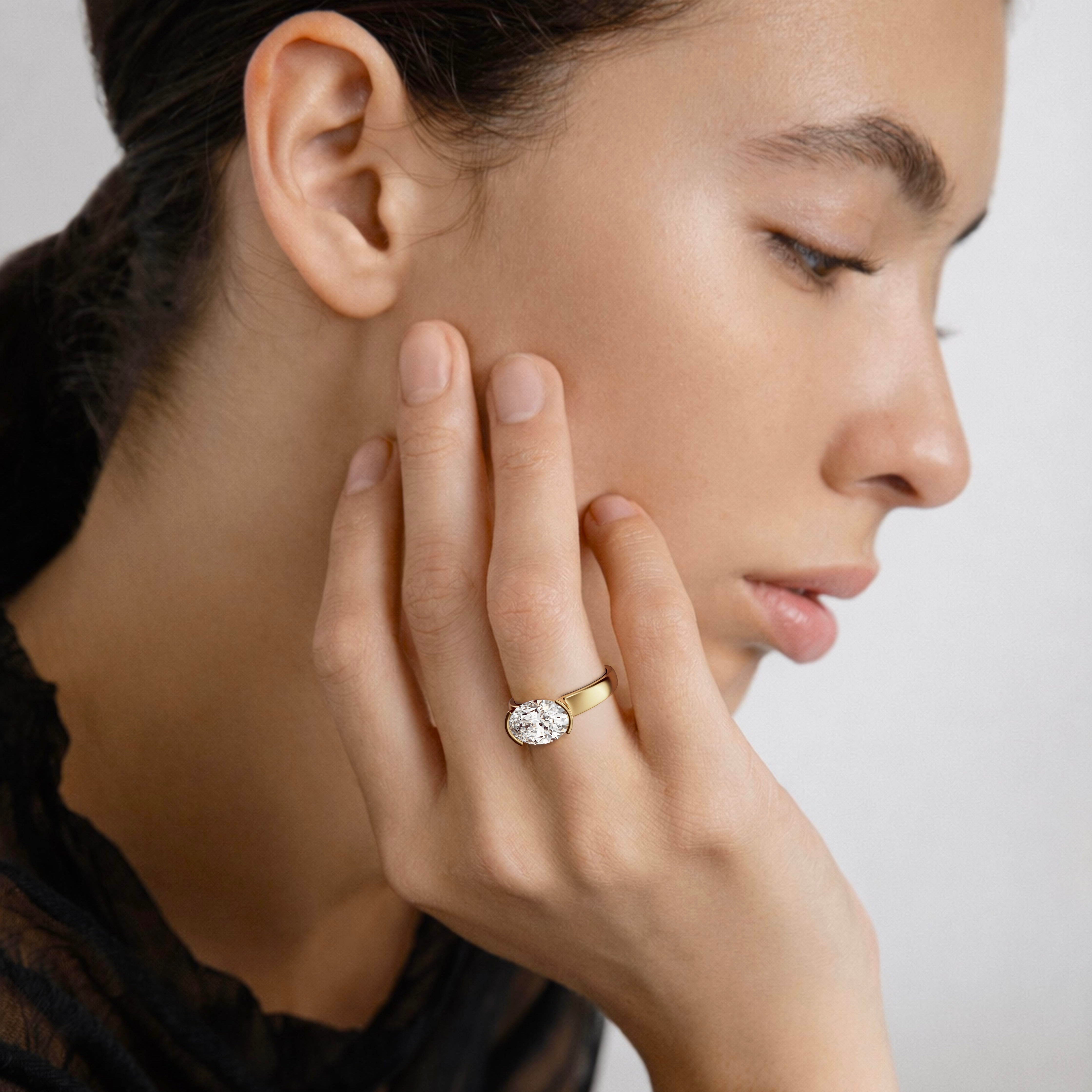 close view of east-west oval diamond engagement ring with tapered partial bezel and narrowing band