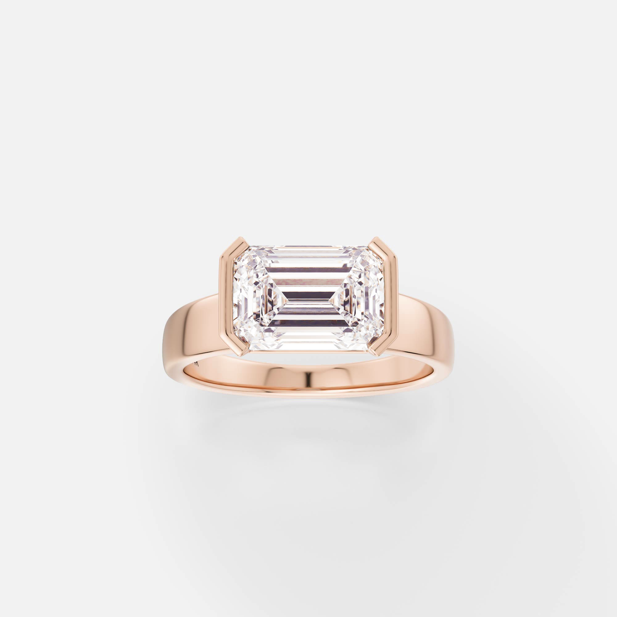 14k rose gold engagement ring with 2.75 carat east-west emerald cut diamond set in tapered partial bezel