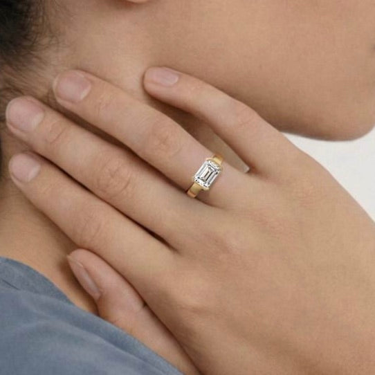 2.75 carat east-west emerald cut diamond engagement ring with tapering partial bezel worn on hand