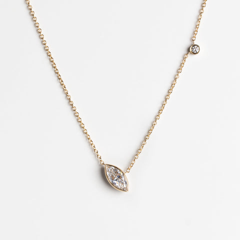 A delicate gold chain necklace featuring a marquise-cut lab-grown diamond pendant and a small round bezel-set round lab-grown diamond on the chain, displayed against a clean white background.
