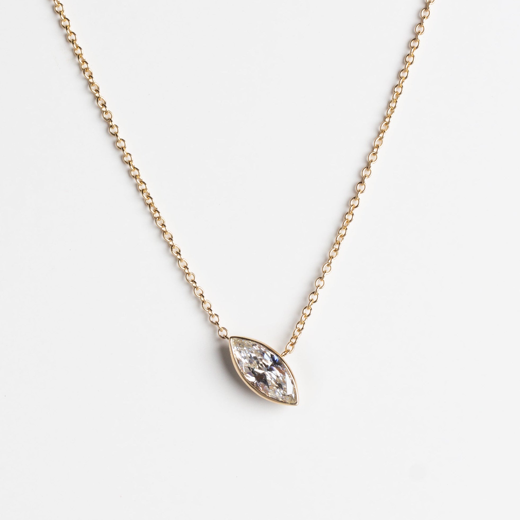 A delicate gold chain necklace featuring a  marquise-shaped pendant set with a lab-grown white diamond, displayed against a clean, light gray background.