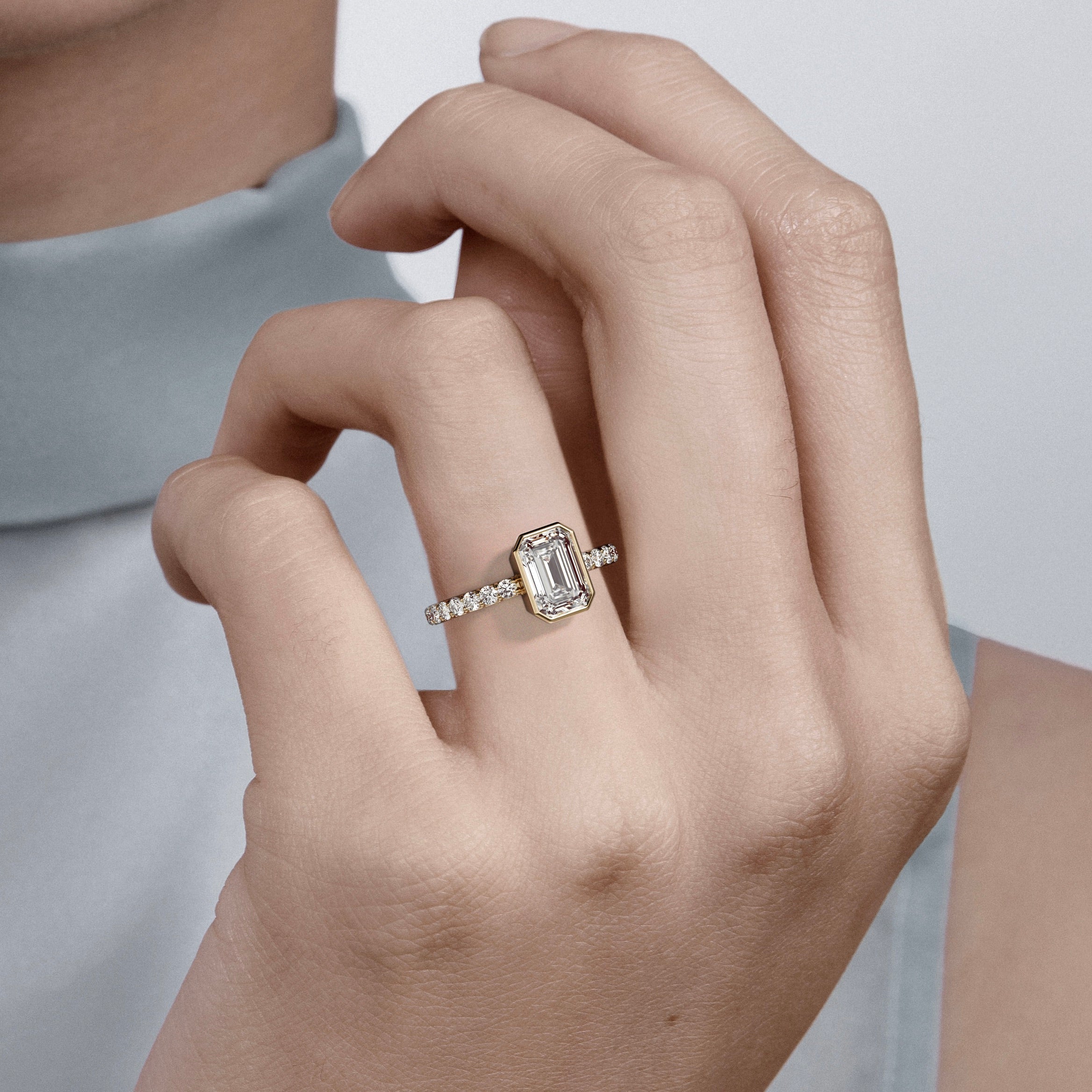 Close view of emerald-cut diamond bezel engagement ring with pavé diamond band