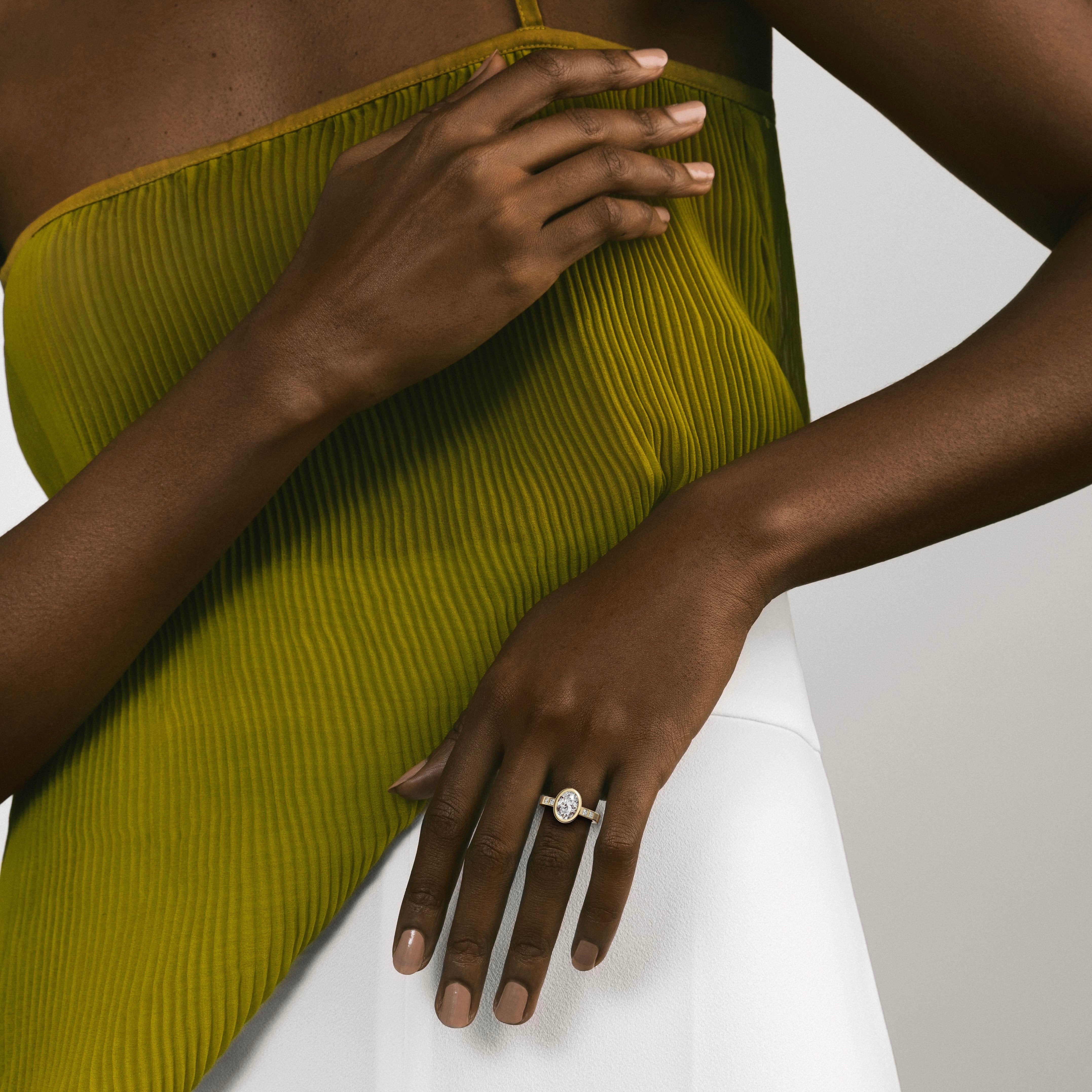 oval diamond engagement ring with princess-cut diamonds set along the band worn on hand